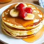 Fluffy pancakes stacked high on a plate, drizzled with maple syrup and topped with fresh berries