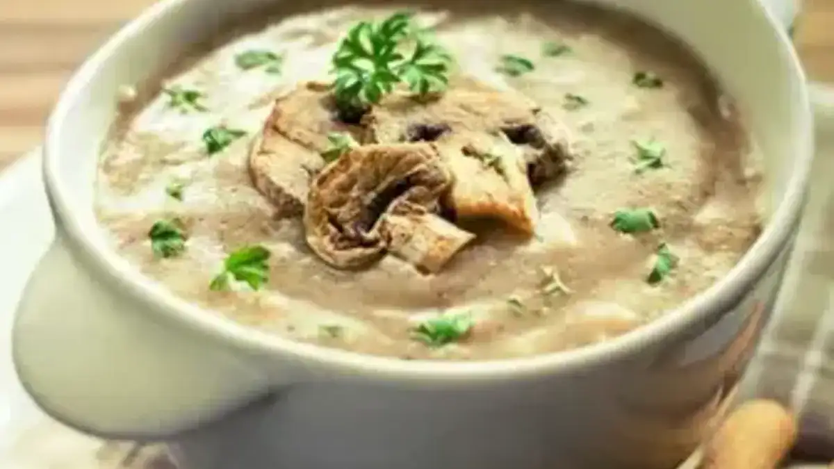 "Bowl of creamy mushroom soup garnished with fresh herbs and served with a slice of crusty bread."