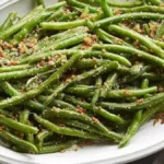 Vibrant green beans sautéed with garlic and topped with toasted almonds, served on a white plate