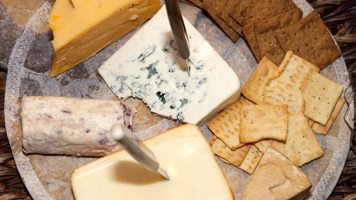 An assortment of Cheese and crackers recipe arranged on a wooden board, garnished with grapes and nuts.