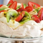 A beautifully arranged Strawberry Pavlova topped with fresh fruits and whipped cream, showcasing its crisp outer shell and soft inner meringue.