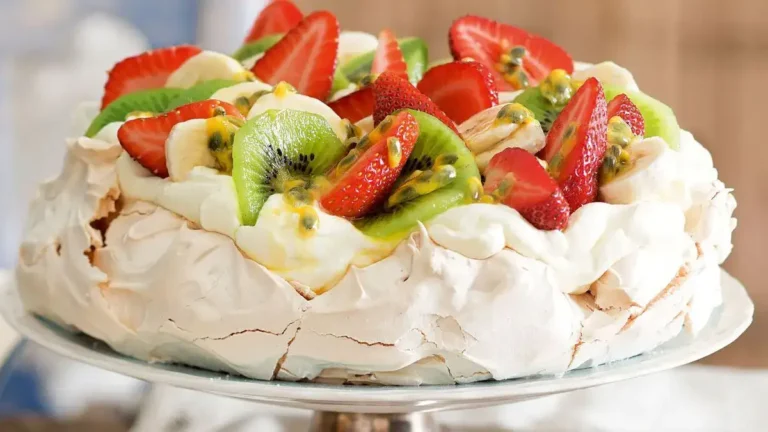 A beautifully arranged Strawberry Pavlova topped with fresh fruits and whipped cream, showcasing its crisp outer shell and soft inner meringue.