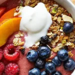 A colorful smoothie bowl topped with fresh fruits, granola, and seeds.