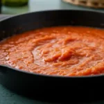 Homemade Salsa Brava simmering in a black cast iron pan, a classic Spanish spicy tomato sauce.