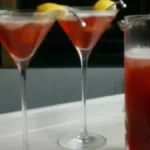 Two Madras cocktails with lemon garnish on a table, next to a pitcher of red drink