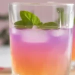 Gradient purple and orange detox drink served with mint leaves in a clear glass.