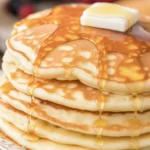 Fluffy buttermilk pancakes stacked on a plate with syrup drizzle.