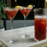 Two Madras cocktails with lemon garnish on a table, next to a pitcher of red drink