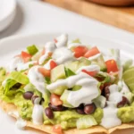 Tostaguac dish featuring a crisp corn shell with guacamole, ground beef, beans, and fresh veggies.