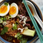A delicious bowl of birria ramen topped with tender beef, rich broth, and fresh herbs.