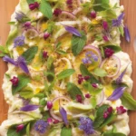 An inviting butter board topped with herbs and spices served with warm bread.