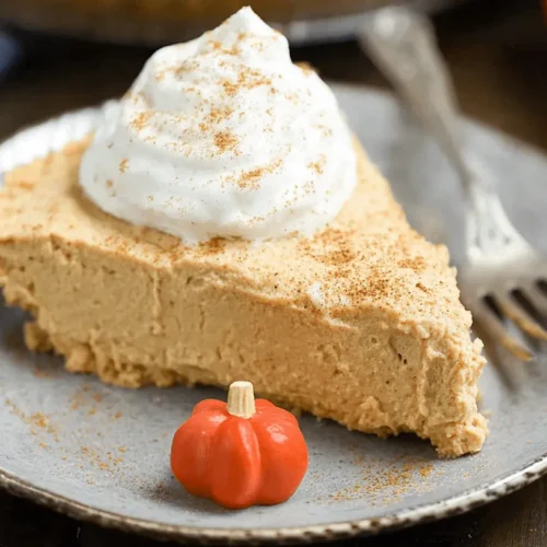 A creamy slice of no bake pumpkin pie topped with whipped cream and spice on a rustic plate.