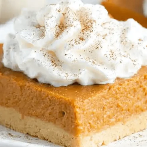 Delicious pumpkin pie bars topped with whipped cream and spice on a white plate.
