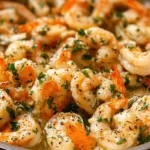 Close-up of a generous serving of perfectly cooked Shrimp Scampi in a metal pan, garnished with fresh parsley and black pepper.